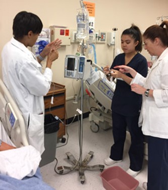 two nursing students in a hospital exam room getting instructions from instructor nurse