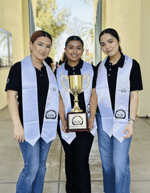 Three students posing wearing stashes and holding a trophy