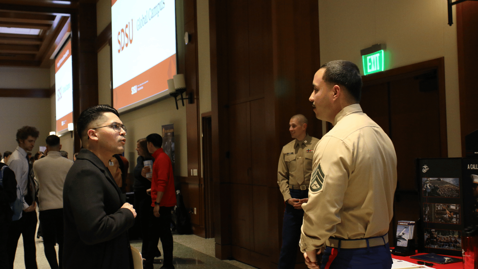 A young male speaking with a military recruiter at a career fair.